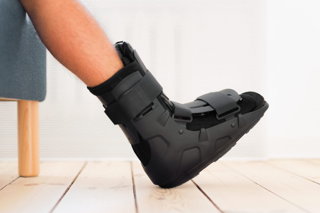 Injury man with black splint on leg sitting on the sofa at home. Ankle foot orthosis close-up.